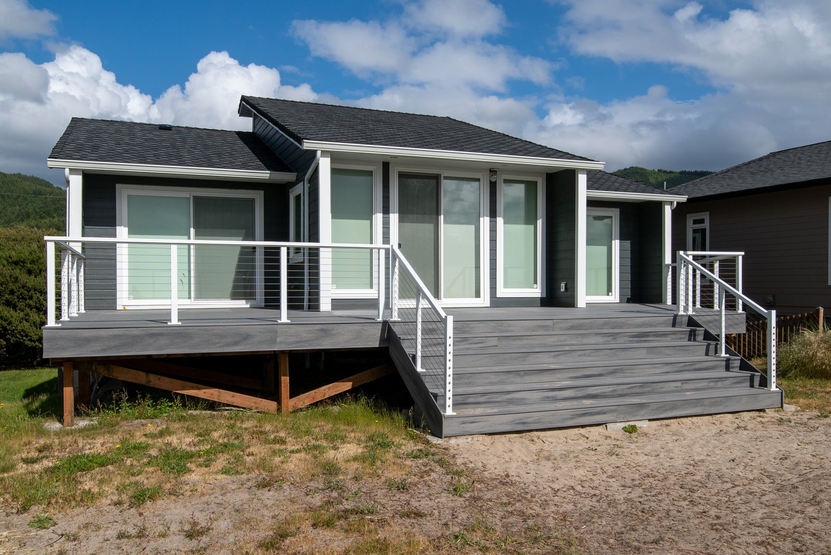 A grey house with a large deck and stairs.