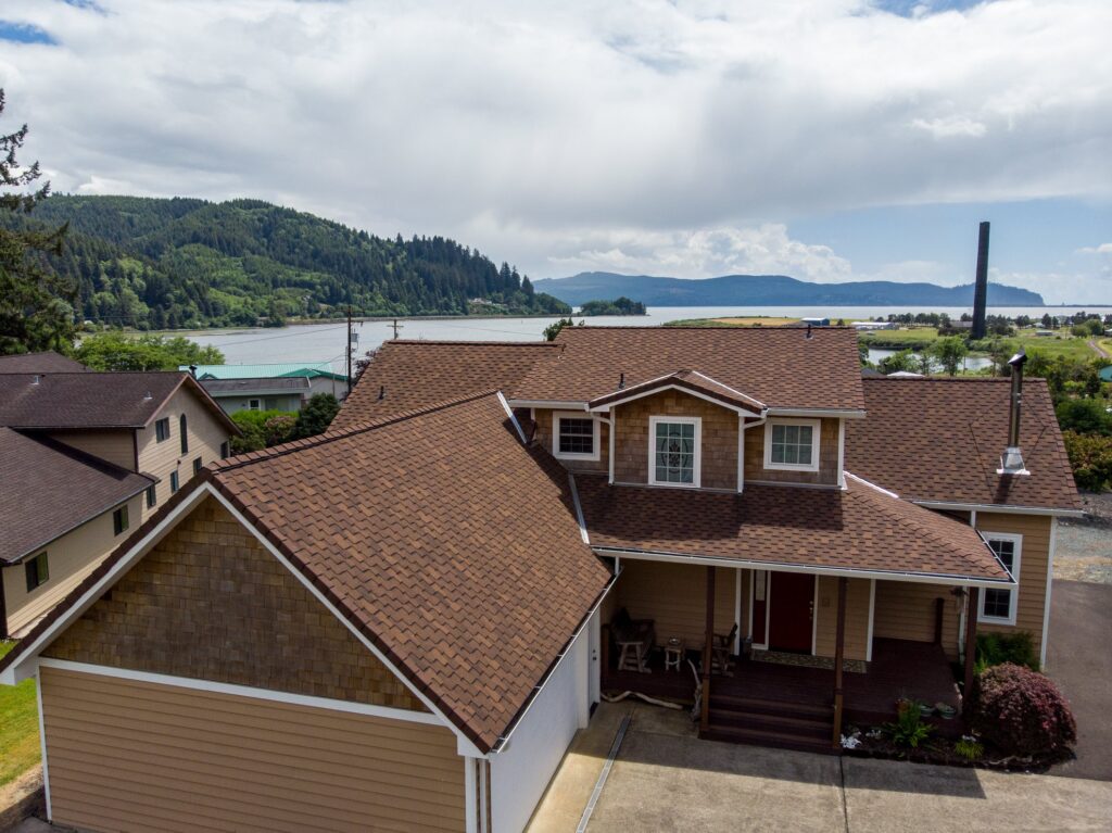 Birds eye view of a house with a brown roof and ocean bay in the background.