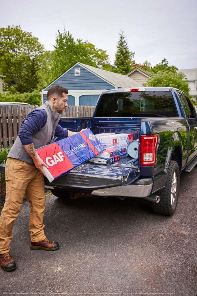 A contractor loading a bundle of GAF shingles into a truck bed.
